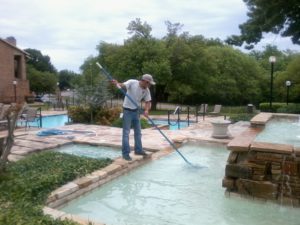 Man who works for a Temecula pool cleaning service brushing a pool